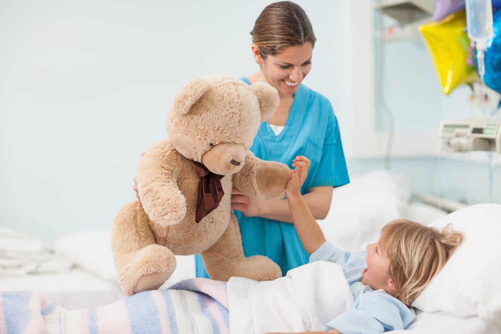 sairaanhoitaja ilahduttaa pientä potilasta nallella Kuva Shutterstock