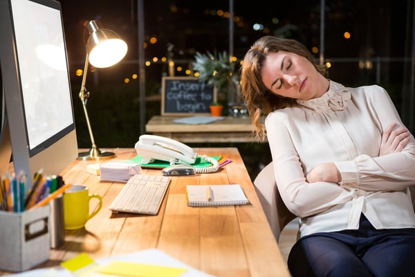 väsynyt nainen nukkuu työpöydän ääressä toimistolla Kuva: Shutterstock