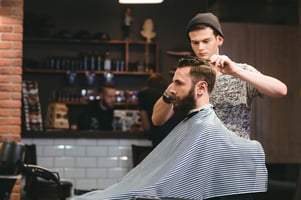 Young handsome barber making haircut of attractive bearded man in barbershop Image: Shutterstock