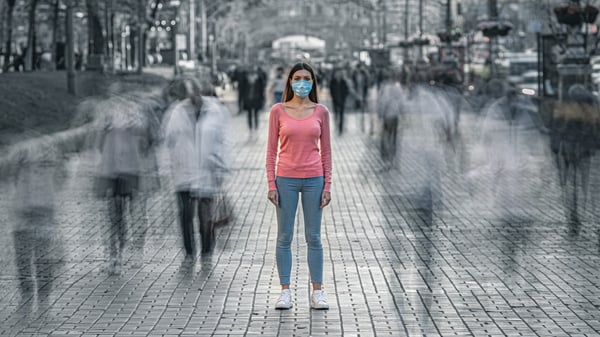 nainen seisoo keskellä ihmisvilinää kasvomaski kasvoillaan AdobeStock